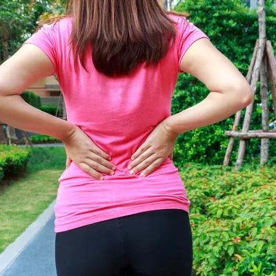 A woman puts her hands on her lower back.