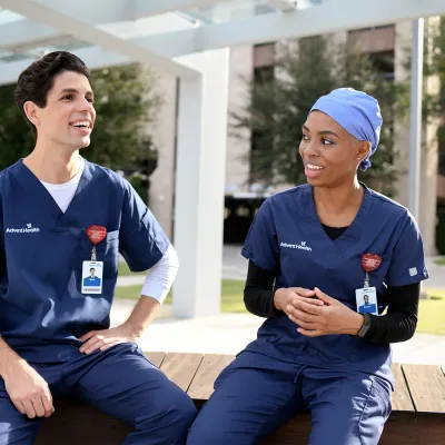 A male nurse sitting outside talking with a female nurse.