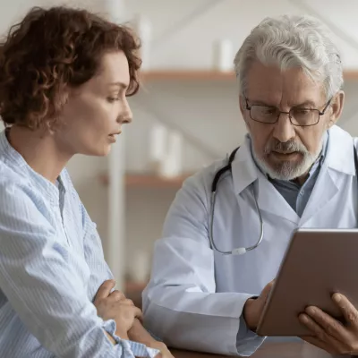 A middle-aged woman and her doctor look at a tablet.