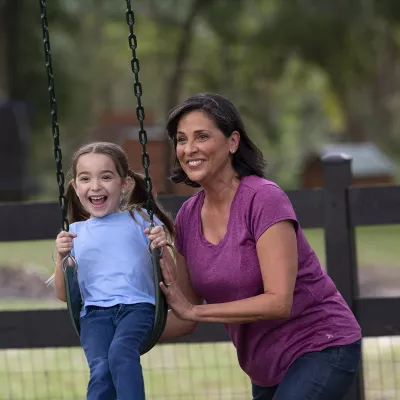 Middle aged woman pushing a little girl on a swing at the park