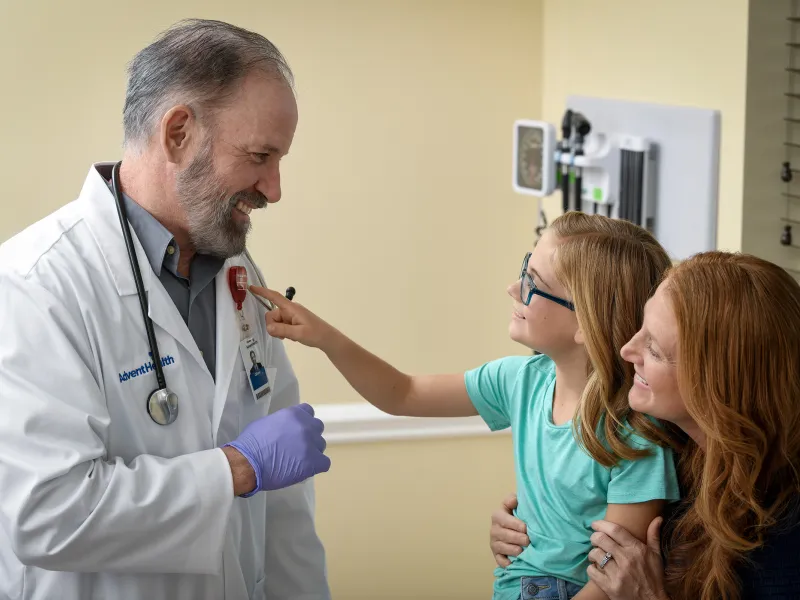 Child sitting on her mother's lap and pointing at doctor's AdventHealth heart badge