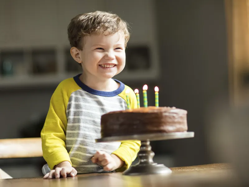 A young boy smiles before blowing out the four candles on his chocolate birthday cake.