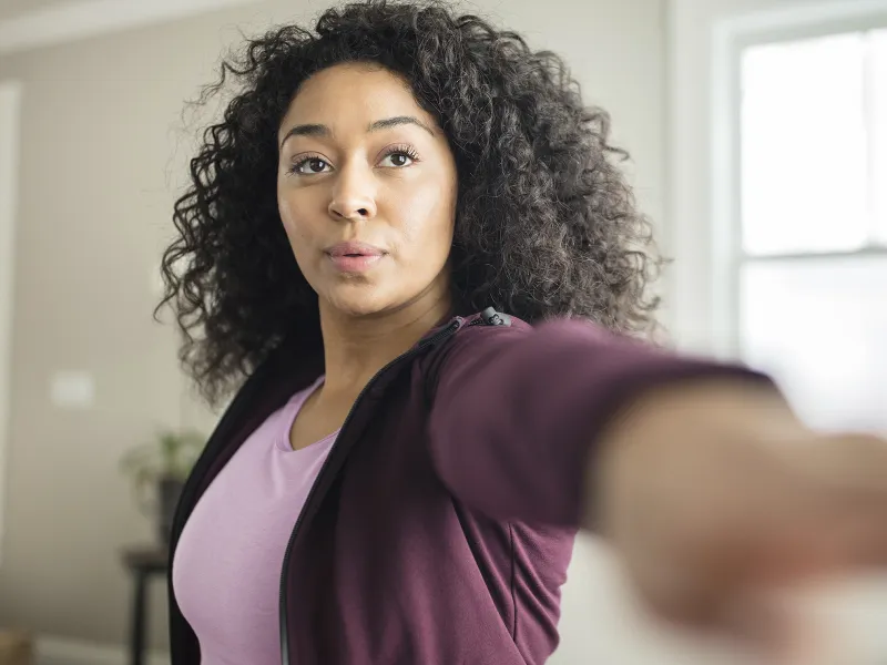 A young African American woman stretches for exercise in her living room.