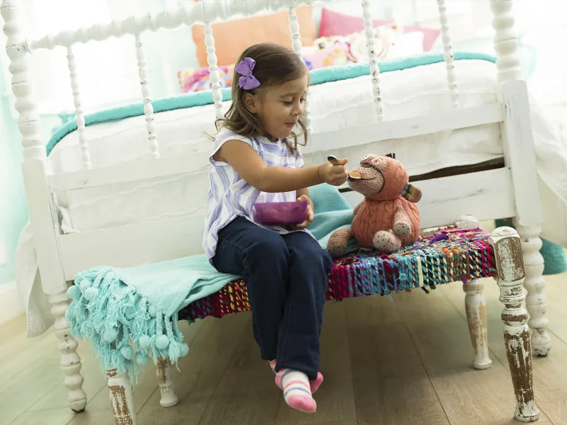 A little girl pretends to feed her stuffed animal in her bedroom