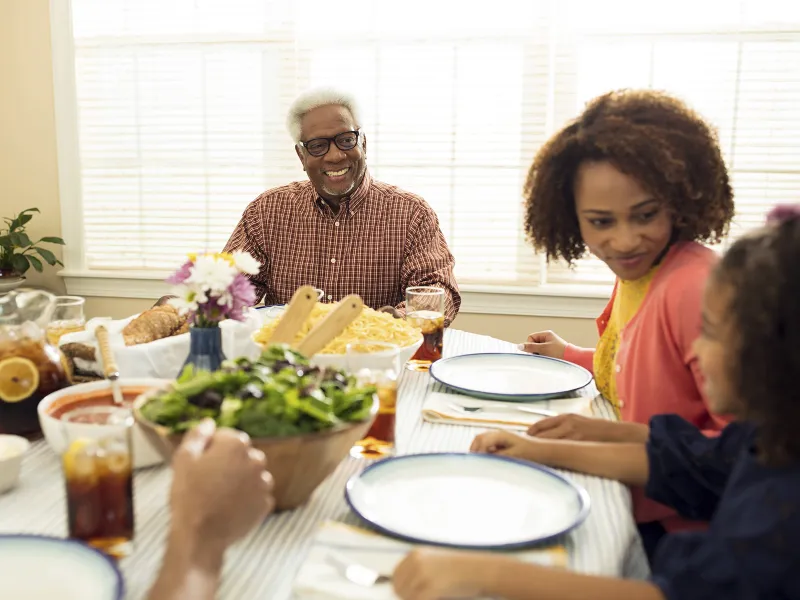 An African American family sits down at the table for a healthy meal.