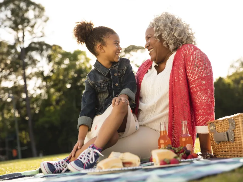 An African American granddaughter and grandmother sit outside for an evening picnic.