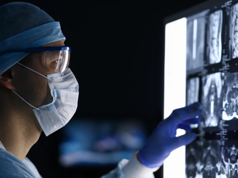 A Doctor, in Full Scrubs and Face Mask, Looks Over His Patient's Scans
