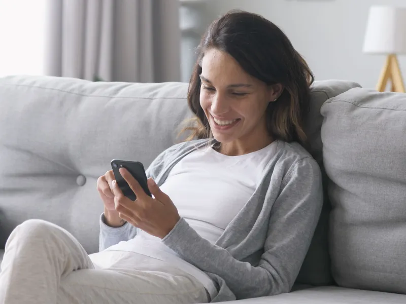 A Woman Sits on Her Couch and Uses Her Smartphone.