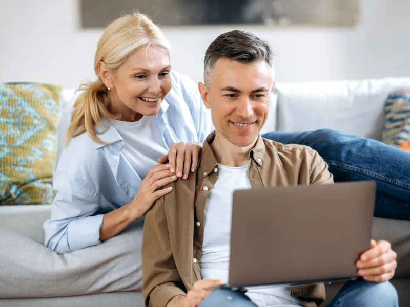 A white mature couple in their living room and on their laptop