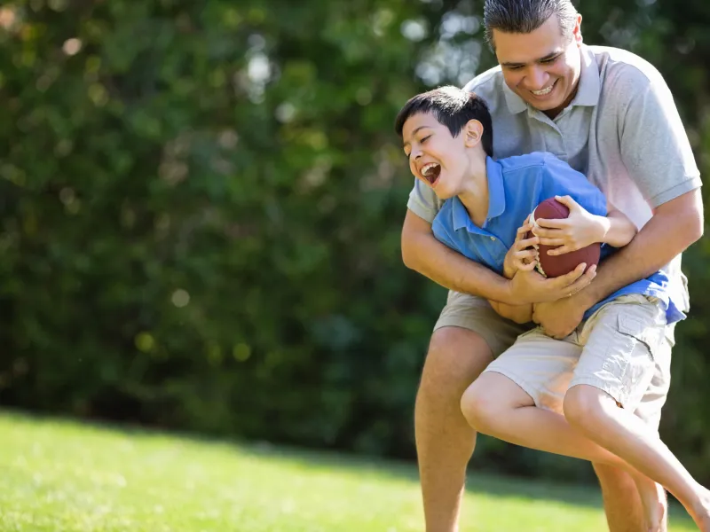 A father and son play football outdoors.