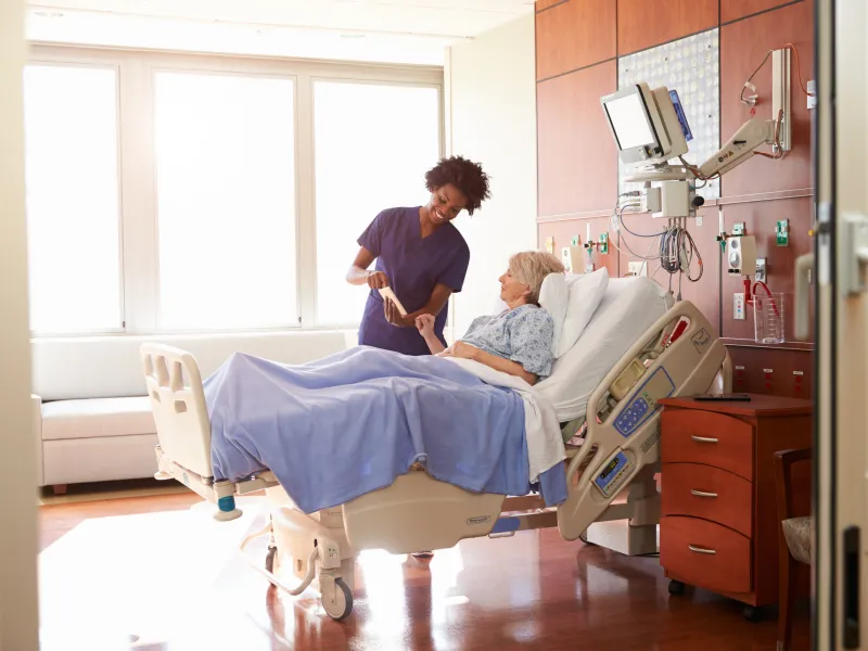 Nurse stands at the bedside of a woman in the hospital.