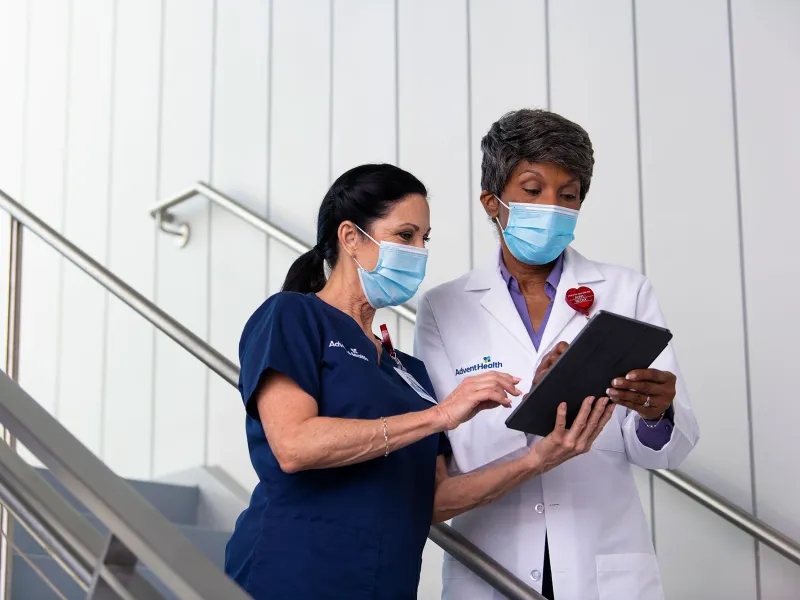 An AdventHealth physician and nurse walking downstairs and talking with tablet