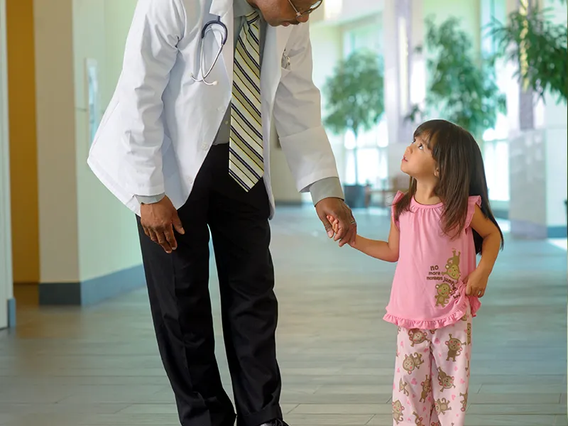A small girl holds her physician's hand in the hallway.
