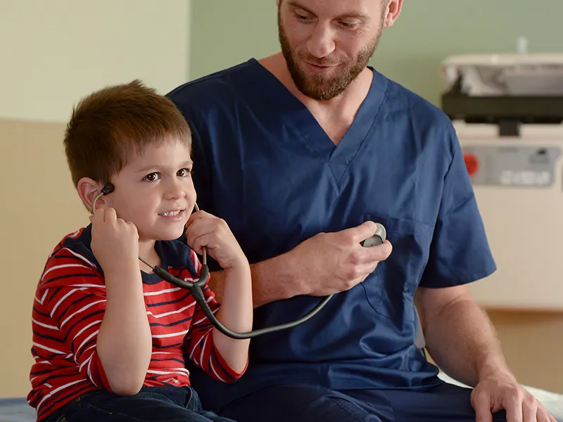 A male nurse lets his child patient listen to a stethoscope.