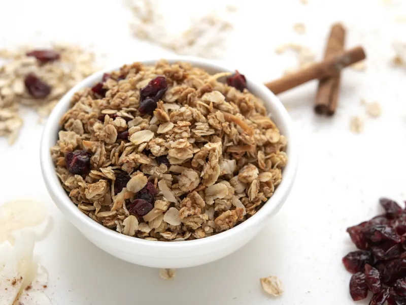 White bowl of granola on white surface with cinnamon stick garnish