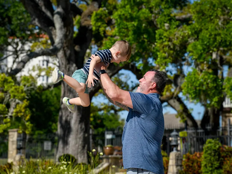 An older father playfully lifts his son in the air