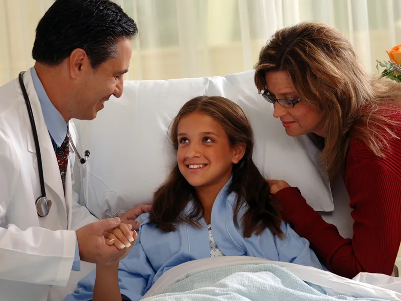 A young patient with her mom holds the hand of her doctor.