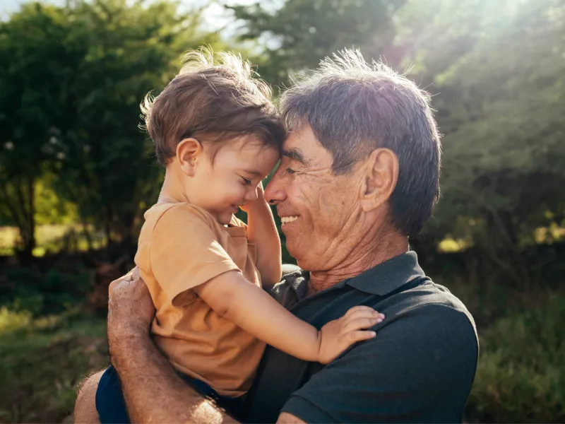 Grandfather holding grandchild while outdoors.