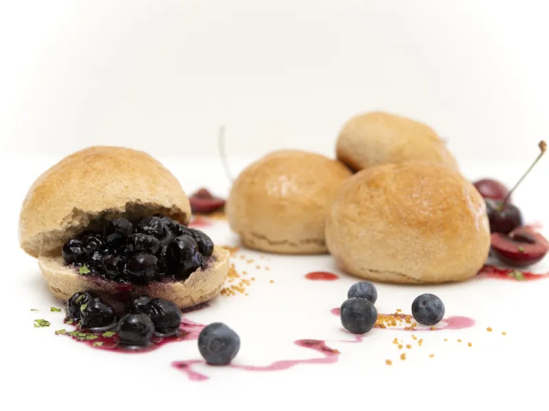four fresh baked rolls, one covered in blueberries with a fruit syrup