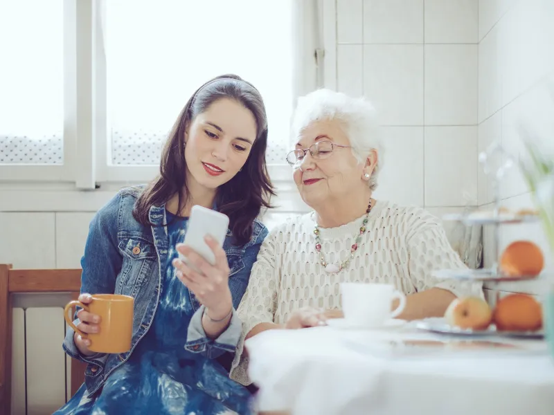 A daughter and her mom sitting at the dining table while looking at the cell phone