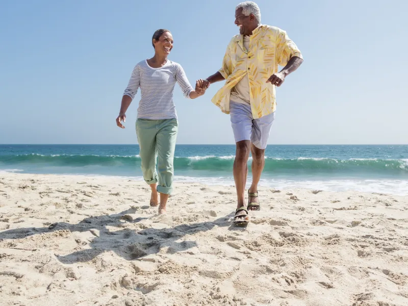 A couple holds hands while walking through sand on the beach.
