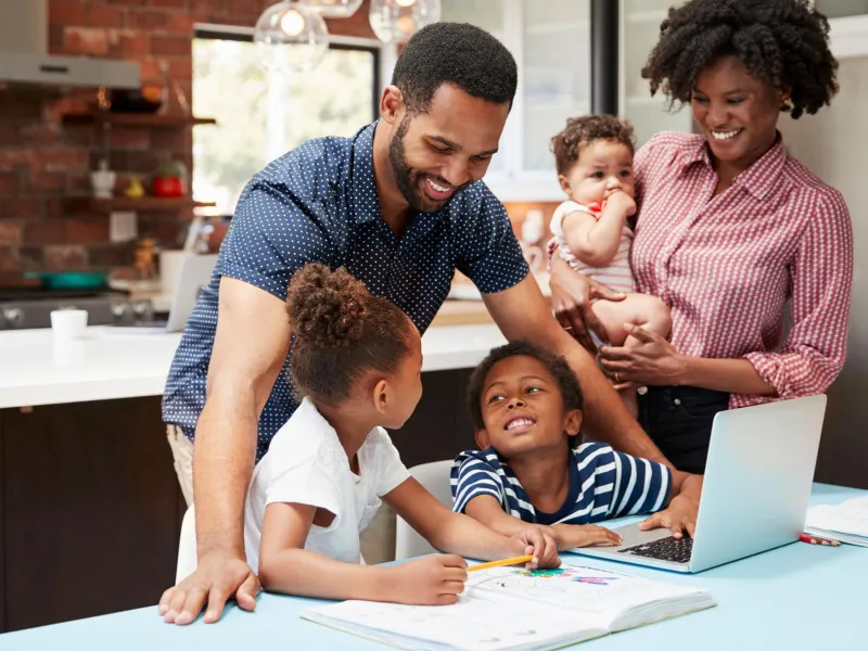 Photo of a family standing at a laptop making plans and smiling.