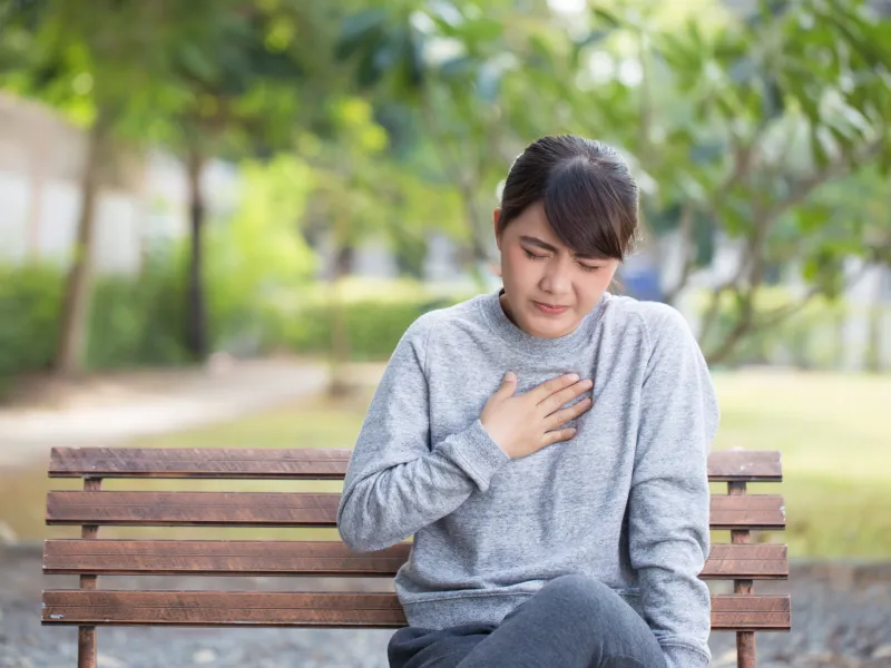 Adult woman experiencing heartburn on a bench outside
