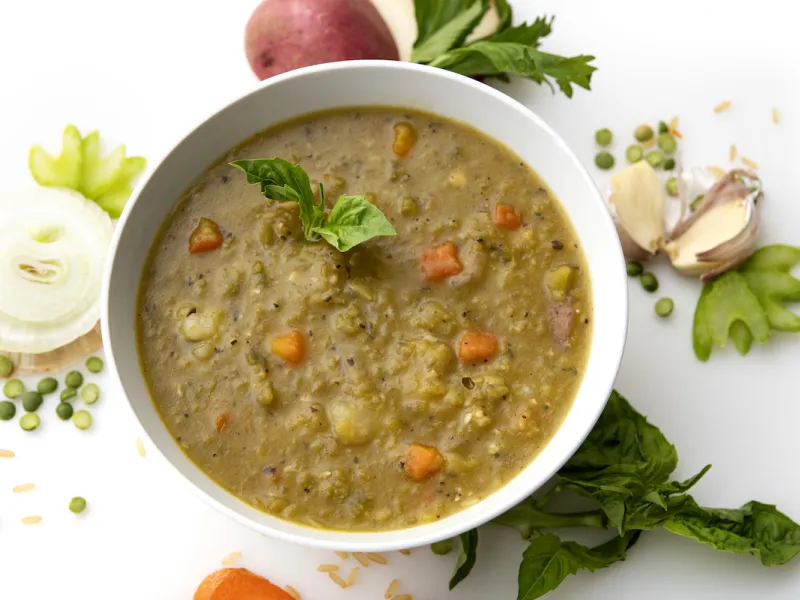 Bowl of split pea soup with onion and green garnishes
