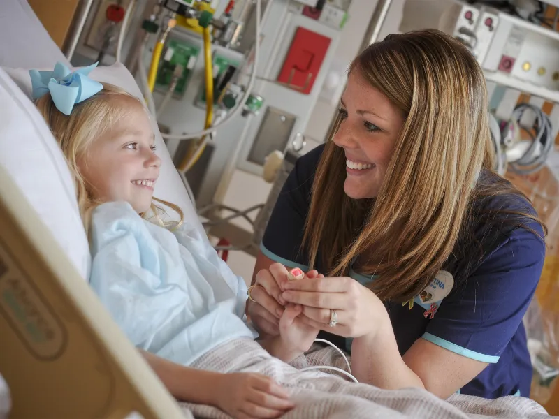 Smiling pediatric nurse with a little girl in a hospital bed