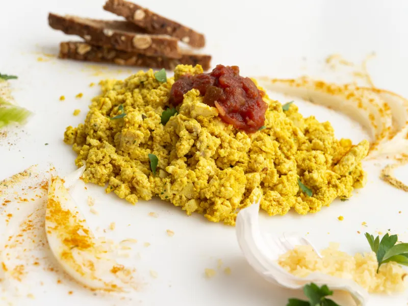 Scrambled tofu on white surface with toast garnish