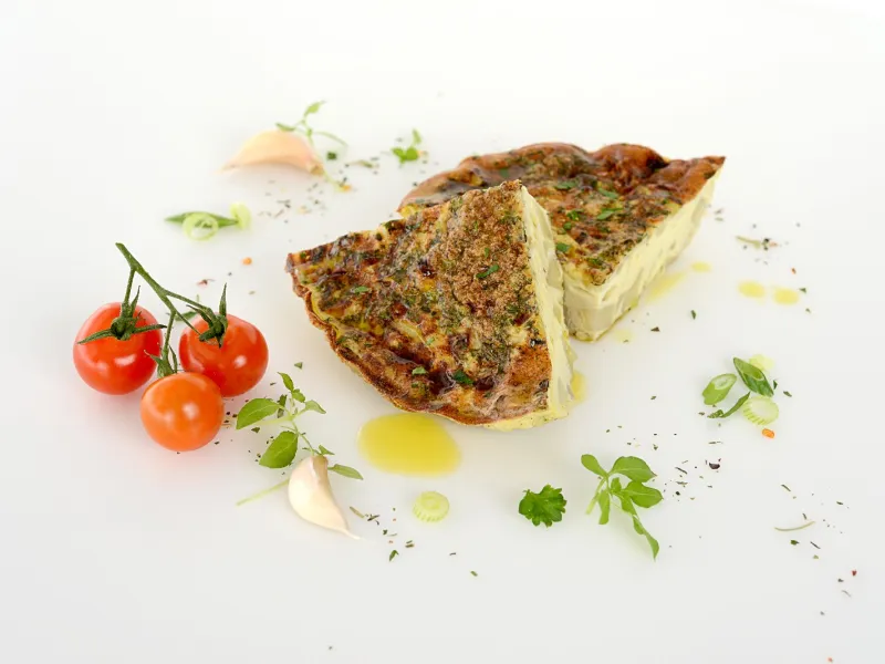 Two triangular eggy potato servings surrounded by tomatoes and herbs