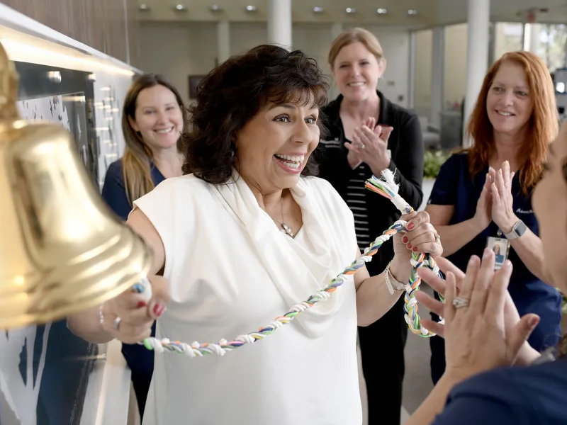 A happy woman ringing the bell at Winter Park Cancer Center.