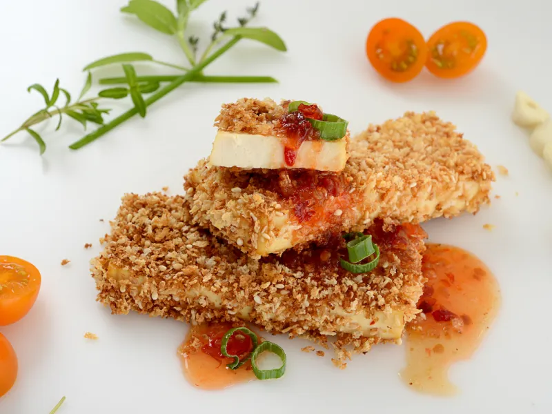 Two and a half crusted tofu steaks with herb and tomato garnishes
