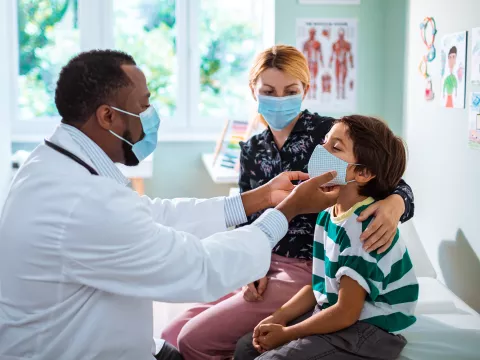 A pediatrician examining a young boy while his mother comforts him on the examination table.