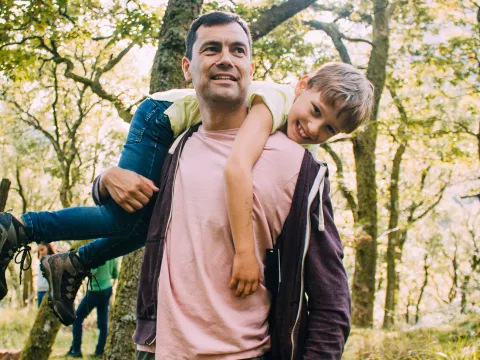 A Man Carrying His Son in a Playful Manner Over His Shoulders Through the Woods.
