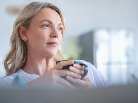An older woman looking contemplative while sipping a cup of coffee.