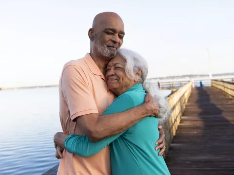 A couple standing on a pier by the lake hugging each other