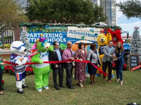 AdventHealth and partners from the Orlando Magic, Florida Citrus Sports, Second Harvest Food Bank and local school districts cut the ribbon on AdventHealth's "Drive Out Hunger" Holiday Bus.