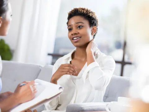A young woman rubs her neck as she talks to a nurse