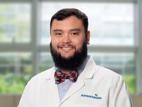 Jacob Parker, a dark-haired, bearded white man in a white medical coat, stands smiling in front of a blurred office-style background.