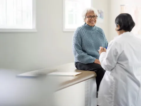 An older female patient talking to a female physician in an exam room.