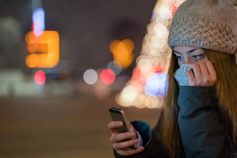 Woman outdoors bundled up in a beautiful winter's evening look at her cell phone