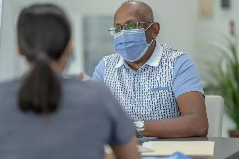A Health Provider Has a Conversation with a Patient in a Clinic Setting While Wear a Mask