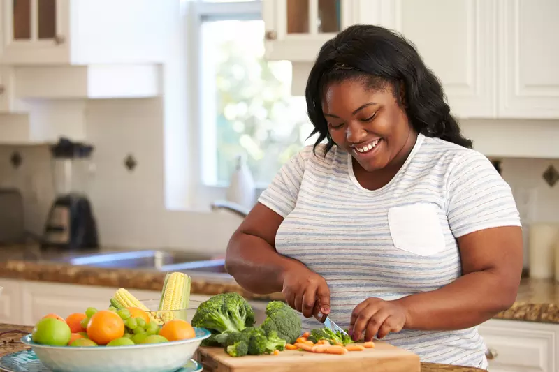 A Woman Chops Vegetables in a Modern Kitchen with a Smile on Her Face.