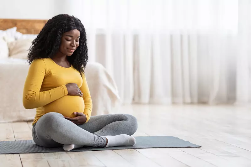 A Woman Sits on a Yoga Mat In Her Bedroom Embracing Her Pregnant Belly.