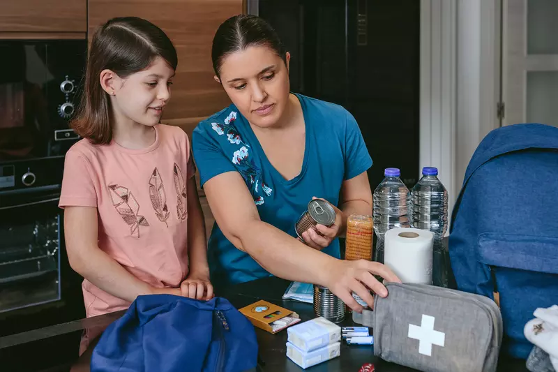 A Mother Looks Over a First Aid Kit with Her Daughter on the Kitchen Table.