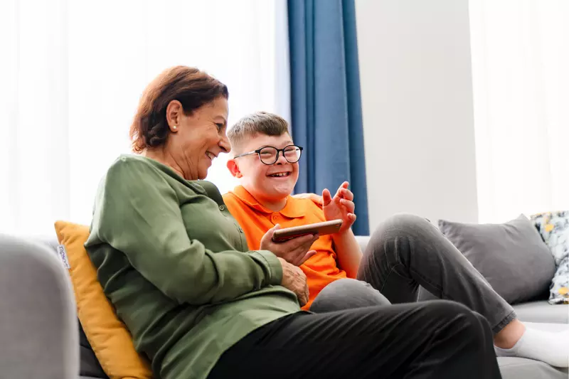 A Child with Down Syndrome Smiles While he and his Mother Look at Content on an iPad