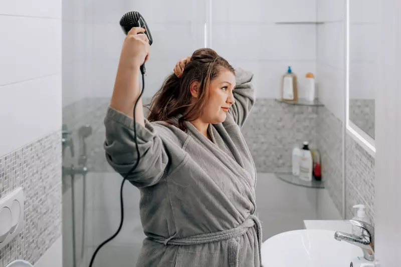 A Woman Blow Dries Her Hair in the Bathroom Mirror