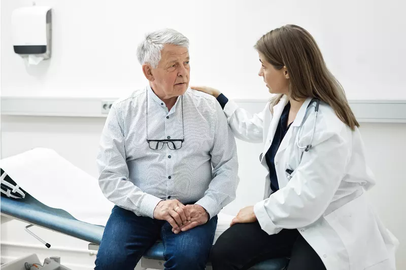 A Doctor Speaks Comfortingly With Her Senior Patient in an Exam Room 