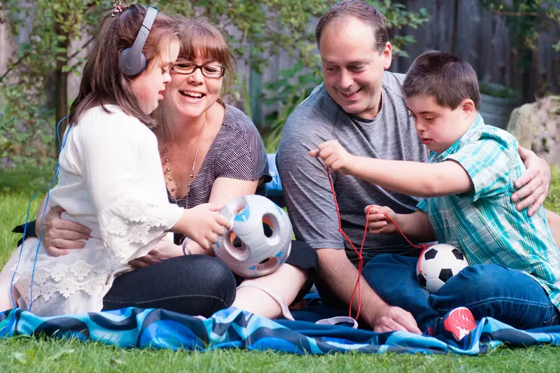 A family of four sitting on a blanket outside, playing with a soccer ball.